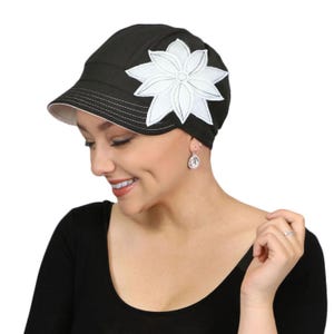 Puede incluir: Gorra negra con una aplicación de flor blanca. La gorra tiene una visera corta y un interior blanco. La flor es un diseño estilizado con múltiples pétalos. Un accesorio elegante.