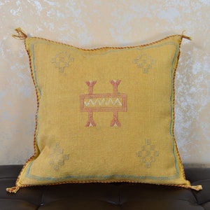 May include: A yellow throw pillow with a geometric pattern in pink and white. The pillow has tassels on the corners.
