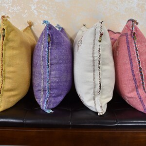 May include: Four decorative throw pillows with embroidered details. The pillows are in shades of yellow, purple, white, and pink.