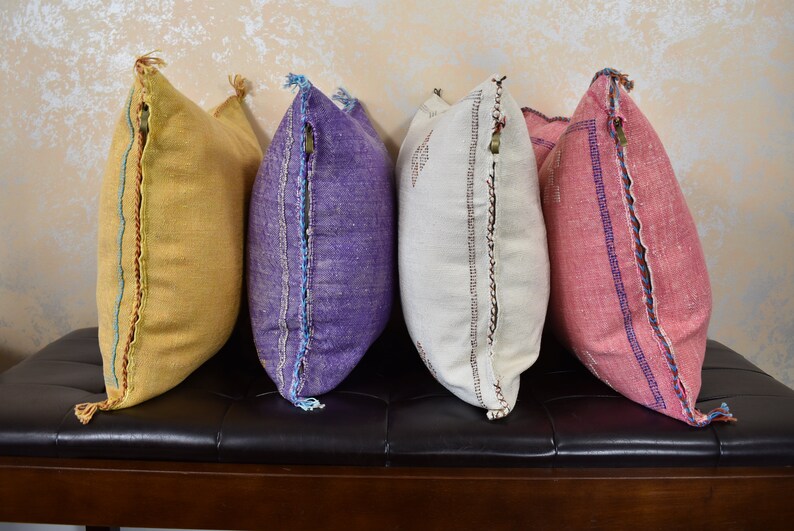May include: Four decorative throw pillows with embroidered details. The pillows are in shades of yellow, purple, white, and pink.