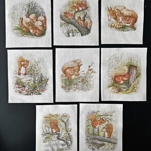 May include: Eight fabric squares with vintage illustrations of squirrels. The images show squirrels in different scenes: gathering nuts, on tree branches, and near a wooden door. The illustrations use a palette of browns, greens, and creams, reminiscent of classic children's book art.