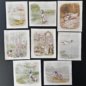 May include: A collection of eight square fabric patches featuring printed illustrations of a duck wearing a blue bonnet and shawl. The scenes depict the duck in various outdoor settings, including a farm, a garden with flowers, and in flight.