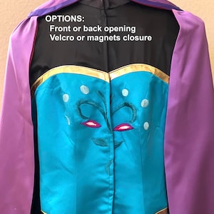 May include: A turquoise blue dress with gold trim and a purple cape. The dress has a floral design on the back and the text "OPTIONS: Front or back opening Velcro or magnets closure".