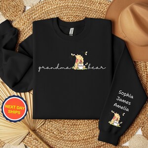 May include: Black sweatshirt with the words "grandma bear" in cursive, and a graphic of a bear holding a honey pot. The sleeve has the names Sophia, James, and Amelia. A round sticker says "NEXT DAY SHIPS".