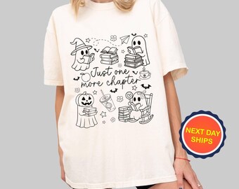 May include: Cream-colored t-shirt featuring a black and white graphic of reading ghosts, a pumpkin, and books. The text "Just one more chapter" is also included in the design. The shirt has short sleeves and a relaxed fit.