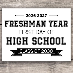 May include: A white sign with black text on a wooden background. The sign reads "2026-2027 FRESHMAN YEAR FIRST DAY OF HIGH SCHOOL CLASS OF 2030". The text is in a bold, collegiate font.