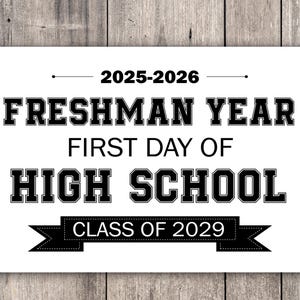 May include: A white sign with black text on a wooden background. The sign reads "2025-2026 FRESHMAN YEAR FIRST DAY OF HIGH SCHOOL CLASS OF 2029". The text is in a bold, collegiate font.