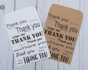 May include: Two small gift bags with the words "Thank you" printed on them in various sizes and fonts. The bags are made of brown and white paper.