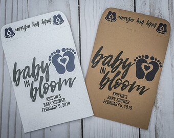 May include: Two brown paper envelopes with the text "baby in bloom" printed in black. The envelopes have a small footprint design with a heart in the center. The text "Kristin's Baby Shower February 9, 2019" is printed below the main text.