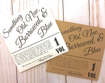 May include: Two cream and brown paper cards with the text "Something Old, New, Borrowed, & Blue" and "1 Vol" printed on them. The text is in a black font. The cards are on a white wooden background.