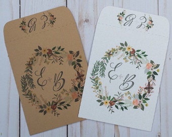 May include: Two wedding favor envelopes with a floral wreath design. The envelopes are brown and white with the initials "E & B" and "G & J" printed on them.