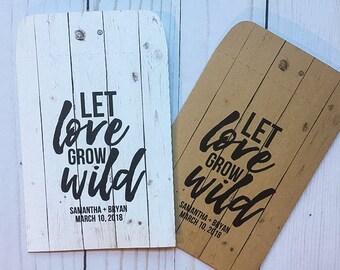 May include: Two wedding favor envelopes with a wood grain background. The envelopes are white and brown. The text on the envelopes reads "Let love grow wild" with the wedding date and couple's names below.