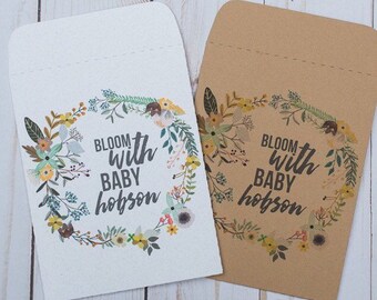 May include: Two brown and white favor bags with a floral wreath design and the text "Bloom with Baby Hobson".