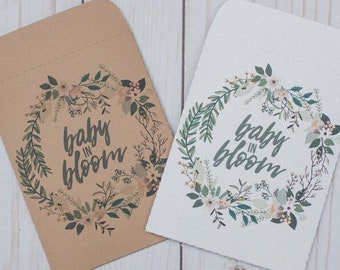 May include: Two kraft paper envelopes with a floral wreath design and the text "baby in bloom".