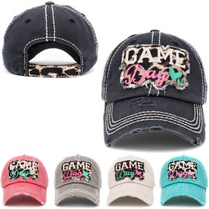 May include: Five distressed baseball caps with the text "GAME DAY" in pink and green lettering. The caps are in black, red, gray, beige, and turquoise.
