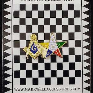 May include: A gold-tone metal lapel pin featuring a Masonic square and compass with a blue G, overlapping a five-pointed star with white, green, red, and blue enamel details, mounted on a black and white checkered display card with text.