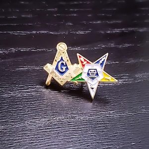 May include: Gold-toned Masonic pin featuring a compass and square with the letter "G" in the centre, and a five-pointed star with a compass and square in the centre.