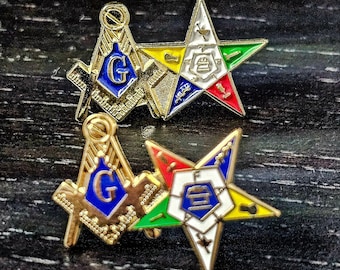 May include: Two gold-tone metal lapel pins featuring a square and compass emblem with a blue center and the letter G, paired with a five-pointed star emblem containing various colored enamel sections, white centers, and small symbolic icons.