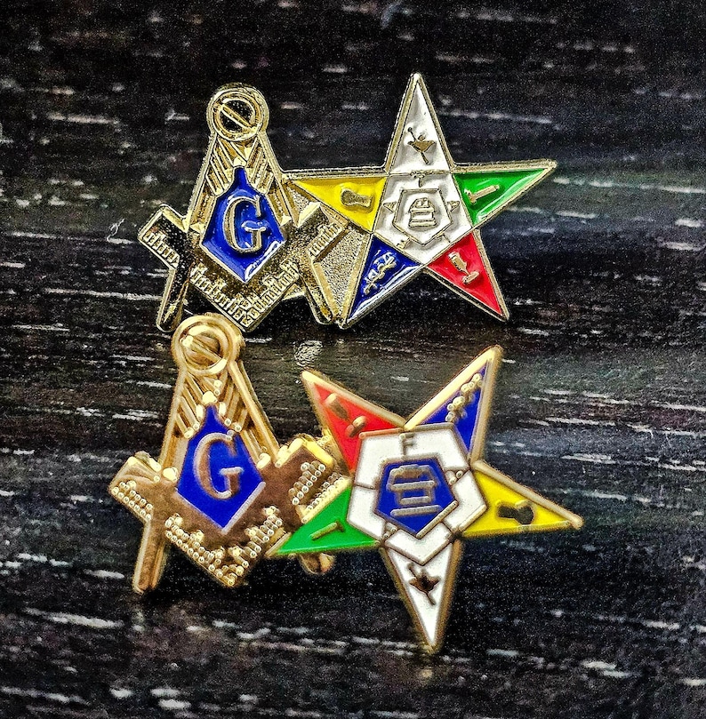 May include: Two gold-tone metal lapel pins featuring a square and compass emblem with a blue center and the letter G, paired with a five-pointed star emblem containing various colored enamel sections, white centers, and small symbolic icons.