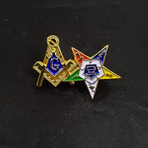 May include: A gold-tone metal lapel pin featuring a Masonic square and compass symbol with a blue center and the letter G, overlapping a five-pointed star emblem with white, blue, green, red, and yellow enamel sections and the letters F, A, T, A, L.