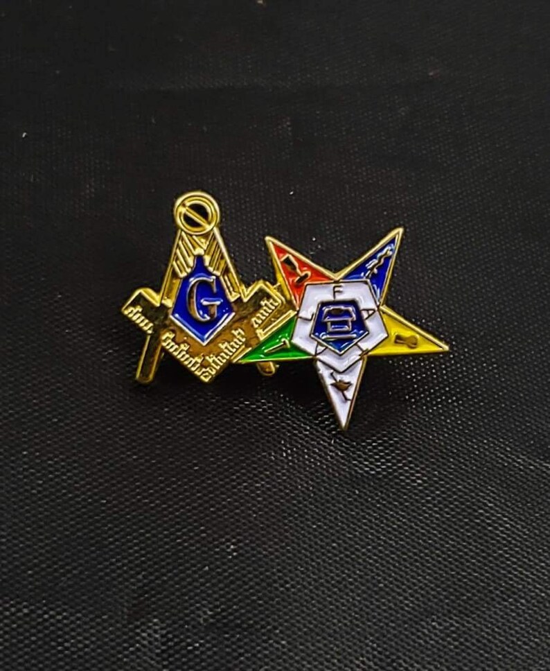 May include: A gold-tone metal lapel pin featuring a Masonic square and compass symbol with a blue center and the letter G, overlapping a five-pointed star emblem with white, blue, green, red, and yellow enamel sections and the letters F, A, T, A, L.