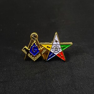May include: A gold-tone metal lapel pin featuring a Masonic square and compass emblem with a blue center and the letter G, joined to a five-pointed star with white, yellow, green, blue, and red enamel sections containing various small symbols.