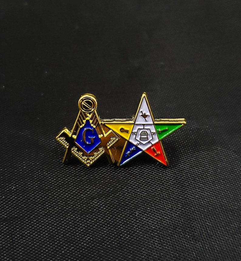 May include: A gold-tone metal lapel pin featuring a Masonic square and compass emblem with a blue center and the letter G, joined to a five-pointed star with white, yellow, green, blue, and red enamel sections containing various small symbols.