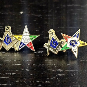 May include: Two gold-tone lapel pins, each featuring a square and compass emblem with a blue center and the letter G, paired with a five-pointed star emblem containing various colored symbols and the letters F, A, and T in a white center.