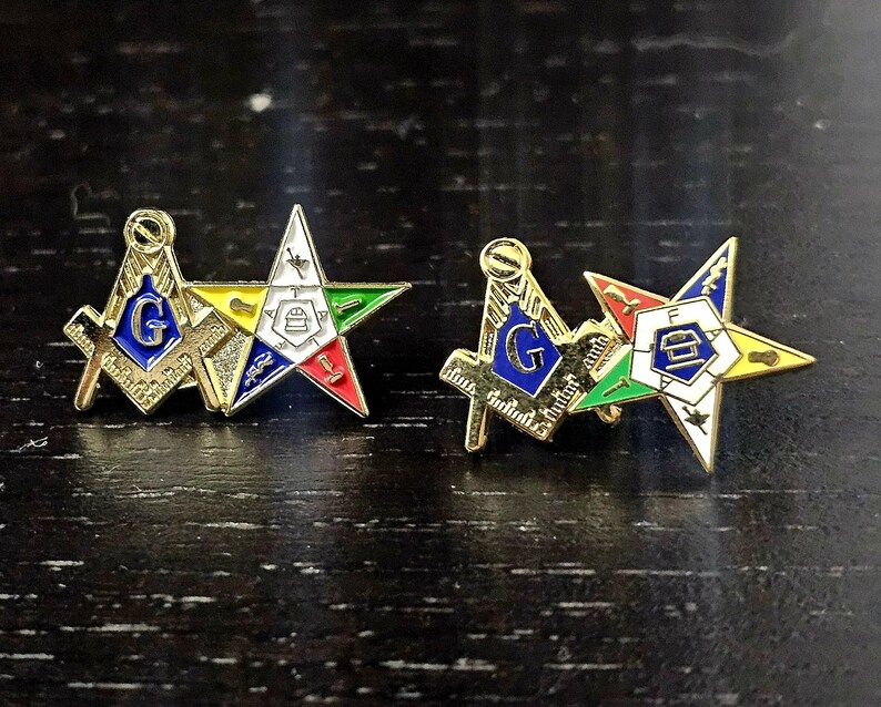 May include: Two gold-tone lapel pins, each featuring a square and compass emblem with a blue center and the letter G, paired with a five-pointed star emblem containing various colored symbols and the letters F, A, and T in a white center.
