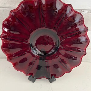 May include: A deep red glass serving bowl with a scalloped edge and a textured design. The bowl is on a black stand.