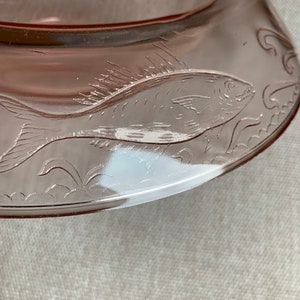 May include: A pink glass serving dish with an etched design of a fish and waves.