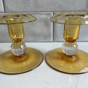 May include: A pair of amber glass candle holders with a textured, clear glass ball base. The holders have a flared top and a cylindrical center.