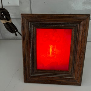 May include: A framed red illuminated picture of a table setting with a centerpiece of teapots and cups.