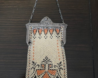 May include: A silver mesh purse with a geometric pattern and orange accents. The purse has a silver chain strap and a beaded fringe.