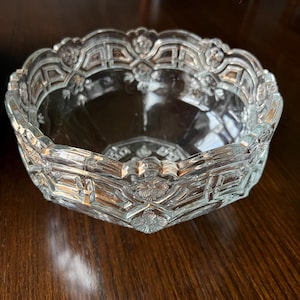 May include: A clear glass bowl with a decorative, geometric pattern around the rim. The bowl has a scalloped edge and is made of clear glass.