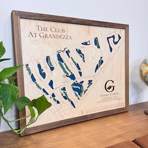 May include: A wooden framed map of The Club at Grandezza golf course in Estero, Florida. The map is laser cut and features a blue and green color scheme. The map includes the course layout, par, yardage, and rating information.