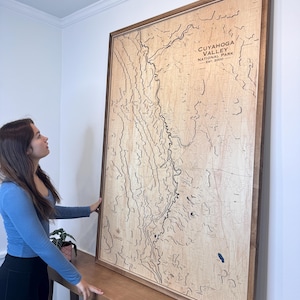May include: A large wooden framed map of Cuyahoga Valley National Park, with the text "CUYAHOGA VALLEY NATIONAL PARK EST. 2000". The map is a light brown color with dark brown lines and details. The frame is a dark brown color.