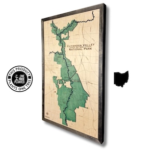 May include: A framed map of the Cuyahoga Valley National Park in Ohio. The map is printed on a vintage-style paper with a green outline of the park. The frame is dark brown wood.