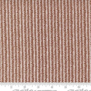 May include: A brown and white fabric with a repeating pattern of small white arrows on a brown background. The fabric is measured with a ruler in inches.