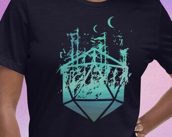 Puede incluir: Una camiseta azul oscuro con un gráfico de una silueta de castillo dentro de un dado de 20 caras con degradado verde y azul. El dado está rodeado por un contorno blanco y dos lunas crecientes.