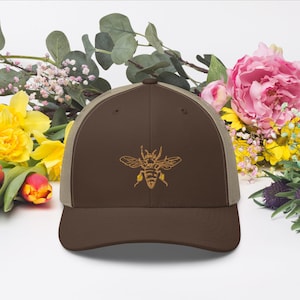 May include: A brown and beige trucker hat with a gold embroidered bee design.