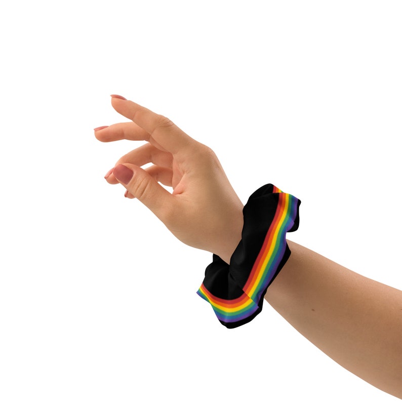 May include: A black scrunchie with a rainbow stripe design. The scrunchie is worn on a person's wrist.