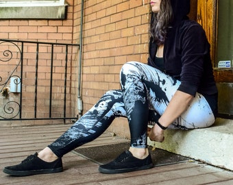 Puede incluir: Una persona con leggings de estampado blanco y negro y una sudadera con capucha negra. La persona está sentada en un escalón con las piernas cruzadas.