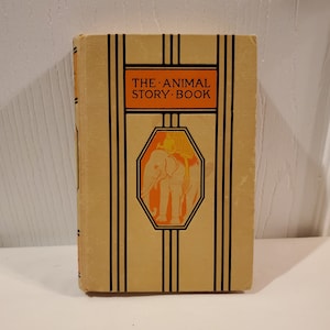 Peut inclure: Un livre vintage intitulé "The Animal Story Book" avec une couverture jaune et des accents noirs et orange. La couverture présente une illustration d'un éléphant avec un cavalier.