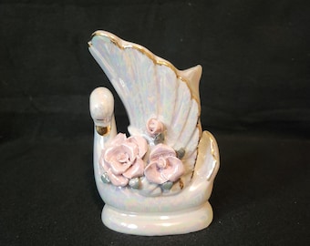 May include: A white porcelain swan figurine with iridescent glaze and gold accents. The swan has pink roses on its back.