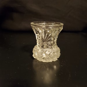Può includere: Un vaso da fiori in vetro trasparente con un motivo a diamante. Il vaso è piccolo e ha un'ampia apertura.