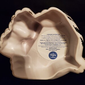 May include: White ceramic decorative bowl with a scalloped edge and black accents. The bowl has a unique shape and a sticker with text that reads "THE GREATEST SHOW ON EARTH".
