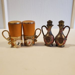 Könnte beinhalten: Vier vintage Salz- und Pfefferstreuer. Zwei sind golden und haben ein florales Design mit roten Akzenten. Die anderen beiden sind braun und haben einen goldenen Rand mit den Worten "Las Vegas" darauf.