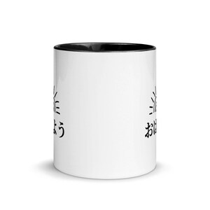 May include: White ceramic mug with a black rim. The mug has a black sun graphic and the Japanese text "おはよう" (good morning) on the left side and "おやすみ" (good night) on the right side.