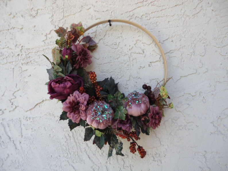 May include: A purple and green floral wreath with glittery pumpkins on a wood hoop